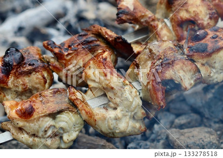 Grilled pieces of mackerel on skewers cooking over hot charcoal, with smoke rising. High quality photo 133278518