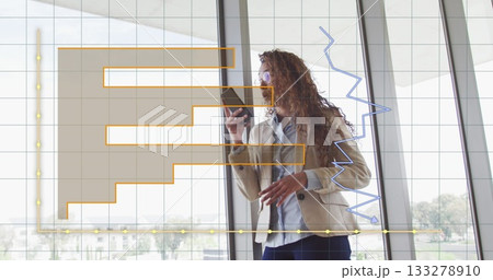 Standing woman in beige blazer reviewing smartphone data by office windows, financial chart overlay Standing woman in beige blazer reviewing smartphone data by office windows, financial chart overlay 133278910