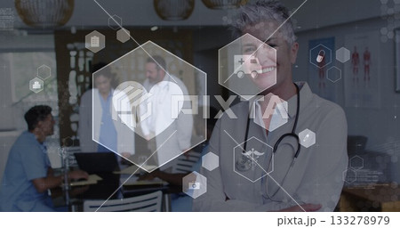 Standing senior female physician crossing arms in clinic room, with laptop charts and medical icons Standing senior female physician crossing arms in clinic room, with laptop charts and medical icons 133278979