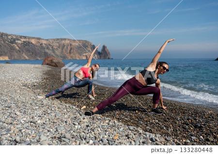 Yoga women stretching fitness exercise routine on remote pebble beach cliffside Yoga women stretching fitness exercise routine on remote pebble beach cliffside 133280448