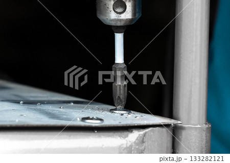 Close-up of electric drill screwdriver driving screw into metal sheet, 133282121