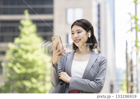 スマホの画面を見るイヤホンをつけたビジネスウーマン スマホの画面を見るイヤホンをつけたビジネスウーマン 133286919