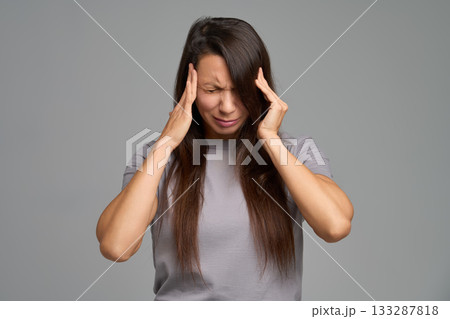 Stressed woman pressing temples during intense headache attack, eyes closed 133287818