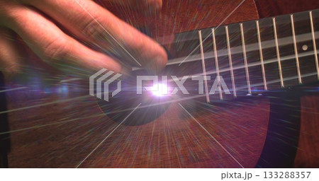 Strumming hand in dark sleeve pressing steel strings on acoustic guitar in studio, with lens flare 133288357