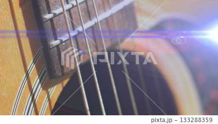 Displaying acoustic guitar with metal strings running across fretboard in studio, with lens flare 133288359