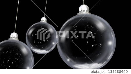 Hanging silver-capped bauble on cord containing star confetti and snow over black void, copy space Hanging silver-capped bauble on cord containing star confetti and snow over black void, copy space 133288440
