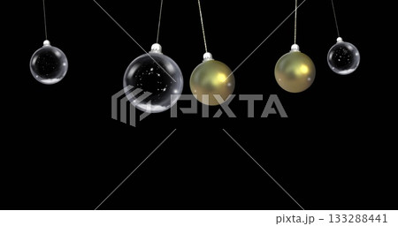 Hanging five Christmas baubles on cords swinging against black backdrop, with gold and star motifs Hanging five Christmas baubles on cords swinging against black backdrop, with gold and star motifs 133288441