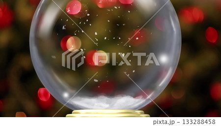 Shining glass snow globe resting on golden base in festive home, showcasing suspended snowflakes 133288458