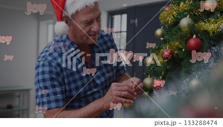 Man in Santa hat attaching gold bauble to Christmas tree at home, Joy overlays, copy space 133288474