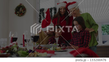 Gathering family wearing Santa hats around table at home, viewing smartphone and dinner dishes 133288476