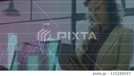 Analyzing mature businesswoman studying data on tablet in office, with chart overlay, copy space Analyzing mature businesswoman studying data on tablet in office, with chart overlay, copy space 133288587