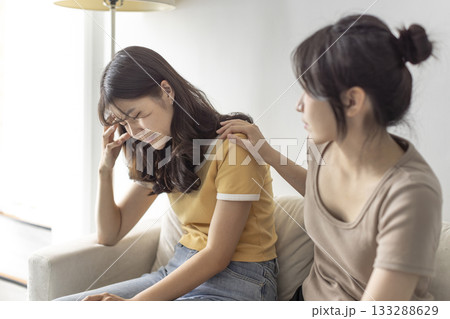 young woman supporting and comforting her sad friend while sitting on the sofa at home. young woman supporting and comforting her sad friend while sitting on the sofa at home. 133288629