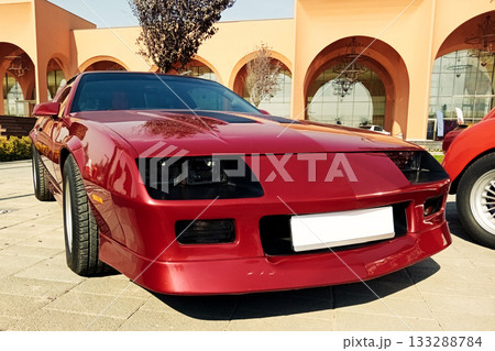 glossy red sports coupe on the paving stones in front of a modern building on a sunny day 133288784