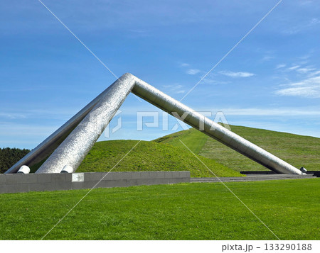 Modern architectural sculpture against a bright blue sky and green landscape	 133290188