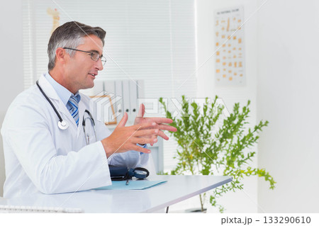 Mature adult male doctor gesturing while explaining diagnosis at desk with stethoscope, copy space Mature adult male doctor gesturing while explaining diagnosis at desk with stethoscope, copy space 133290610
