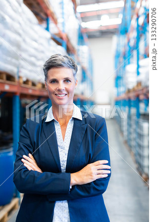 Mature adult woman standing in warehouse aisle wearing navy blazer amid steel racks of white sacks 133290706