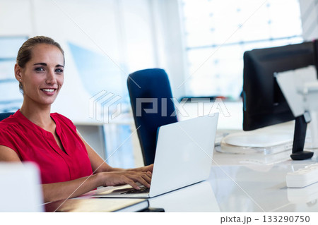 female in red blouse typing on laptop at desk in open office with binder, copy space 133290750