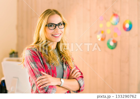 Smiling woman wearing red plaid shirt crossing arms in creative studio with monitor, color swatches Smiling woman wearing red plaid shirt crossing arms in creative studio with monitor, color swatches 133290762