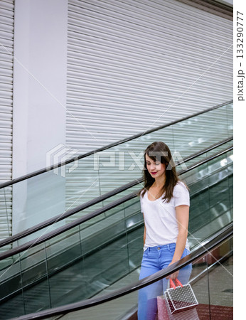 Woman descending moving escalator inside mall carrying polka dot gift bag, copy space Woman descending moving escalator inside mall carrying polka dot gift bag, copy space 133290777