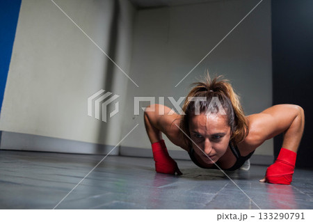 Mid adult woman in sports bra performing low push-up in training room with red wrist wraps 133290791