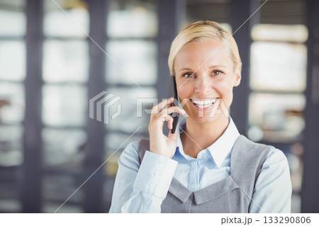 Businesswoman wearing collared blouse and dress carrying smartphone to ear in office, copy space 133290806