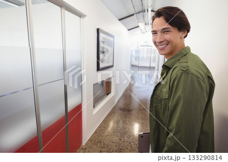 Asian man smiling and holding closed laptop while standing in modern office corridor, copy space Asian man smiling and holding closed laptop while standing in modern office corridor, copy space 133290814