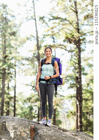Female hiker standing on rock in pine forest gripping poles and carrying purple backpack with pad 133290825