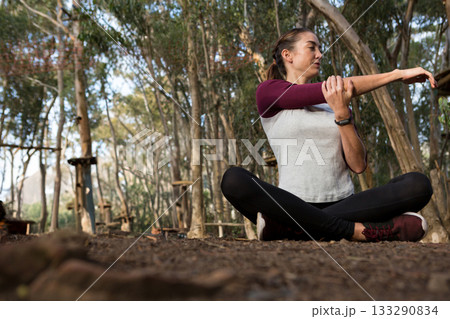 Woman stretching right arm across chest in forest rope course wearing watch, sneakers, copy space 133290834