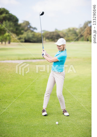 Female golfer swinging driver on golf course fairway with cap glove and golf ball on tee Female golfer swinging driver on golf course fairway with cap glove and golf ball on tee 133290846