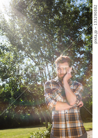Bearded man wearing plaid shirt leaning head crossing arms in park clearing lens flare, copy space Bearded man wearing plaid shirt leaning head crossing arms in park clearing lens flare, copy space 133290882