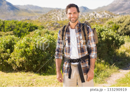 Smiling mid adult man hiking narrow dirt trail with olive-green backpack among distant mountains Smiling mid adult man hiking narrow dirt trail with olive-green backpack among distant mountains 133290919