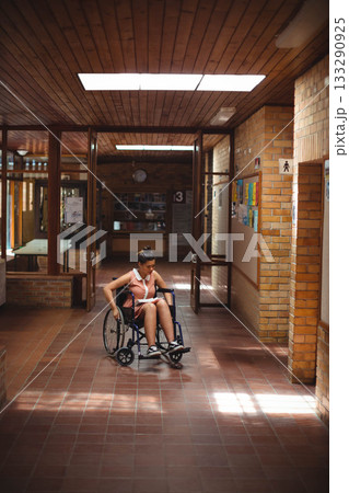 African American teenage student reading notes in notebook in wheelchair in brick-walled hallway 133290925