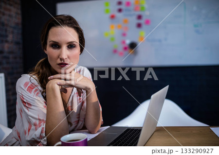 Woman in late twenties leaning over laptop at office with whiteboard with sticky notes, copy space 133290927