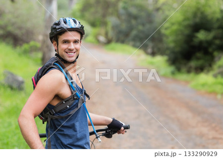 Man smiling while holding bike handlebar on forest trail wearing helmet hydration pack, copy space Man smiling while holding bike handlebar on forest trail wearing helmet hydration pack, copy space 133290929