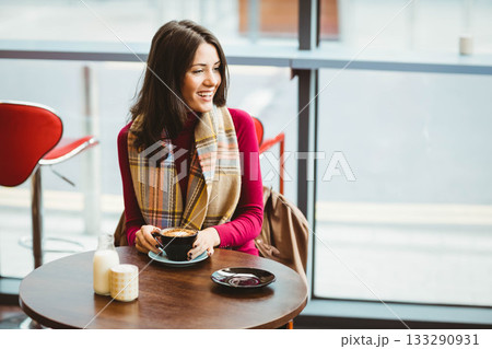 Woman in burgundy turtleneck and scarf sipping cappuccino with milk and sugar jar at café table Woman in burgundy turtleneck and scarf sipping cappuccino with milk and sugar jar at café table 133290931