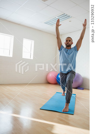 Adult man in T-shirt sweatpants doing lunge on blue mat in yoga room with exercise balls 133290932