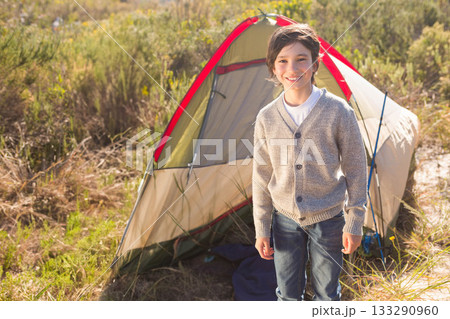 Boy standing and smiling in front of two-person tent at campsite with ground sheet, copy space 133290960