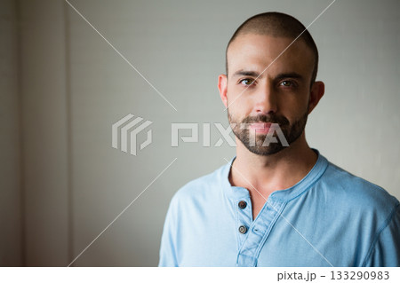 Man standing against smooth painted wall in studio wearing light blue henley shirt, copy space 133290983