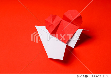 Red origami heart above a white paper plane on red Red origami heart above a white paper plane on red 133291109
