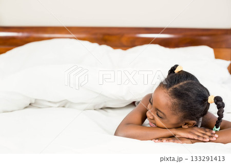 African American child lying on bed smiling amid white pillows and duvet in bedroom, copy space 133291413
