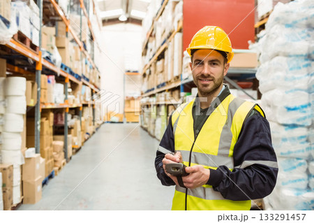 Male warehouse worker wearing vest scanning pallets on racks with scanner in aisle, copy space 133291457