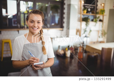 Woman in grey apron writing order on notepad at cafe counter with condiments and napkin holder Woman in grey apron writing order on notepad at cafe counter with condiments and napkin holder 133291499