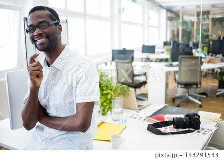 African American man leaning while holding pen at chin in office with DSLR camera, copy space African American man leaning while holding pen at chin in office with DSLR camera, copy space 133291533
