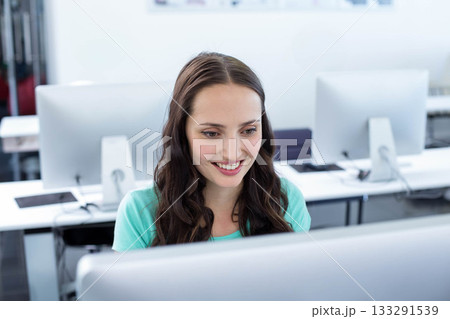 Woman in mid-20s smiling while sitting at computer lab workstation using monitor and keyboard 133291539