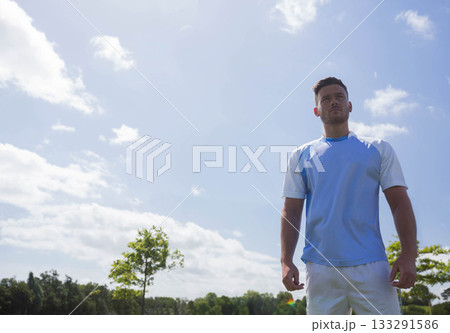 Man standing on sports field wearing athletic jersey and shorts under bright sky, copy space Man standing on sports field wearing athletic jersey and shorts under bright sky, copy space 133291586