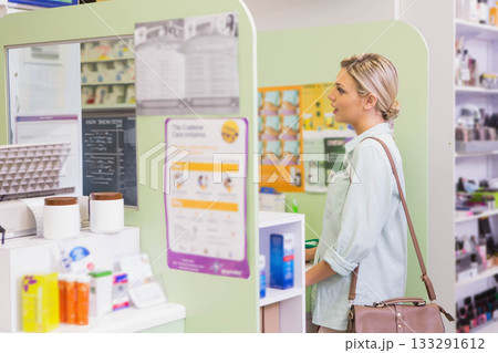 Female customer standing at partitioned counter reading medicine labels, carrying bag, copy space Female customer standing at partitioned counter reading medicine labels, carrying bag, copy space 133291612