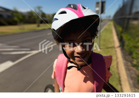African American girl standing on suburban sidewalk wearing white-pink bicycle helmet and backpack African American girl standing on suburban sidewalk wearing white-pink bicycle helmet and backpack 133291615