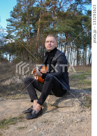 Portrait of smiling caucasian artist plays wooden acoustic guitar in autumnal park. Young songwriter plays string musical instrument hobby outside in nature fall time. Audio music healing Portrait of smiling caucasian artist plays wooden acoustic guitar in autumnal park. Young songwriter plays string musical instrument hobby outside in nature fall time. Audio music healing 133291623