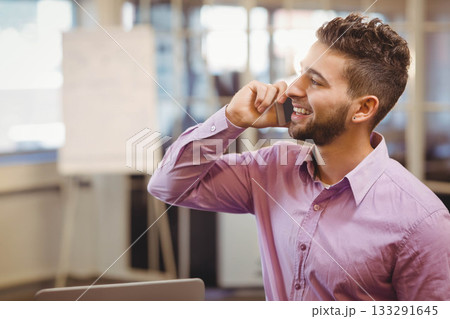 Man wearing shirt and talking on smartphone at office desk with laptop, flip chart, copy space 133291645