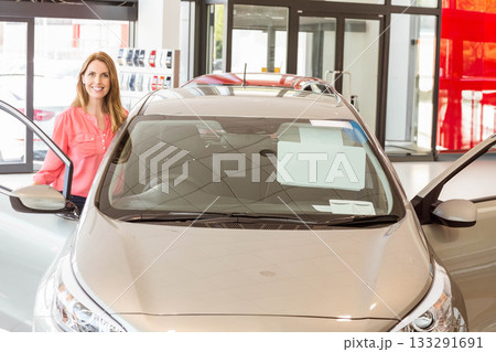 Mid-30s woman inspecting price sheet on silver hatchback windshield at showroom near sample rack Mid-30s woman inspecting price sheet on silver hatchback windshield at showroom near sample rack 133291691